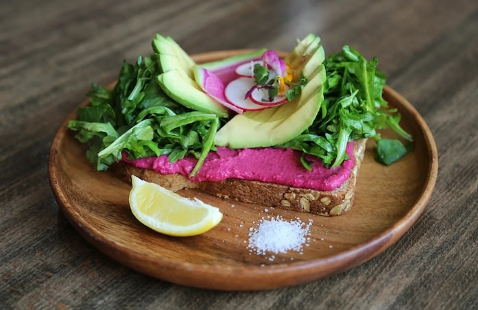 A slice of toast with beetroot hummus, avocado and salad